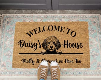 May include: A rectangular doormat made of natural fibers. The mat features the text "WELCOME TO Daisy's House" with a dog illustration. Below the dog, the text reads "Molly & Rover Live Here Too".