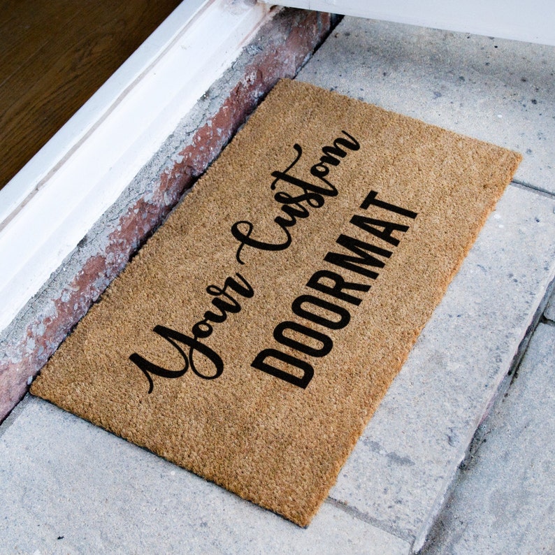 Puede incluir: Una alfombra de coco marr&oacute;n con el texto "Your Custom Doormat" en letras negras cursivas.