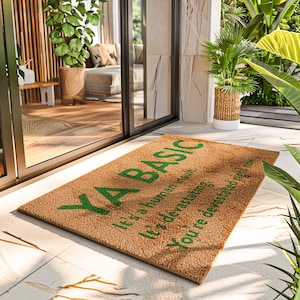 May include: A brown coir doormat with the text "Ya Basic" in green lettering. The text continues with "It's a human trait, it's devastating, you're devastated right now."