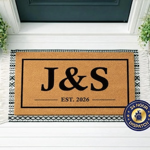 May include: A rectangular doormat with a tan background and a black border. The mat features the letters "J&S" in large black font, with "EST. 2026" below. The mat has a fringed edge.