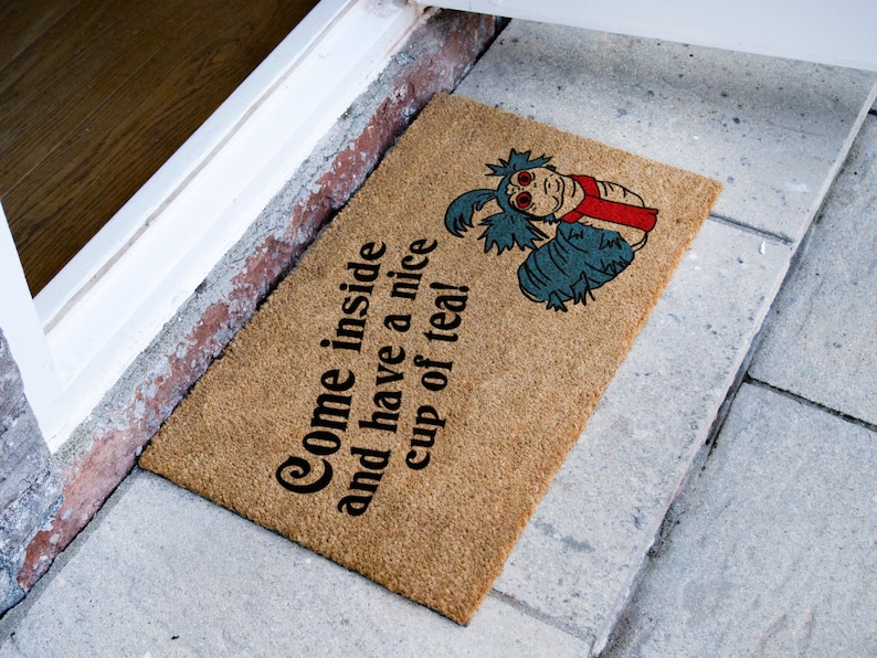 May include: A brown doormat with the text "Come inside and have a nice cup of tea!" and a blue and red cartoon creature.