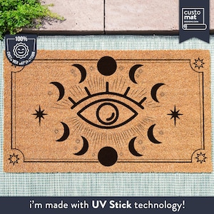 May include: A brown coir doormat with a black and white design of an eye with crescent moons and stars. The text "i'm made with UV Stick technology!" is printed at the bottom of the mat.