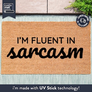 May include: A brown coir doormat with the text "I'M FLUENT IN sarcasm" in black lettering. The doormat is made with UV Stick technology.