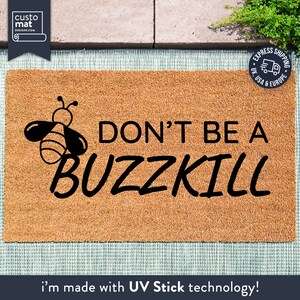 May include: A brown coir doormat with the text "DON'T BE A BUZZKILL" in black lettering. A black cartoon bee with white stripes is to the left of the text. The doormat is made with UV Stick technology.