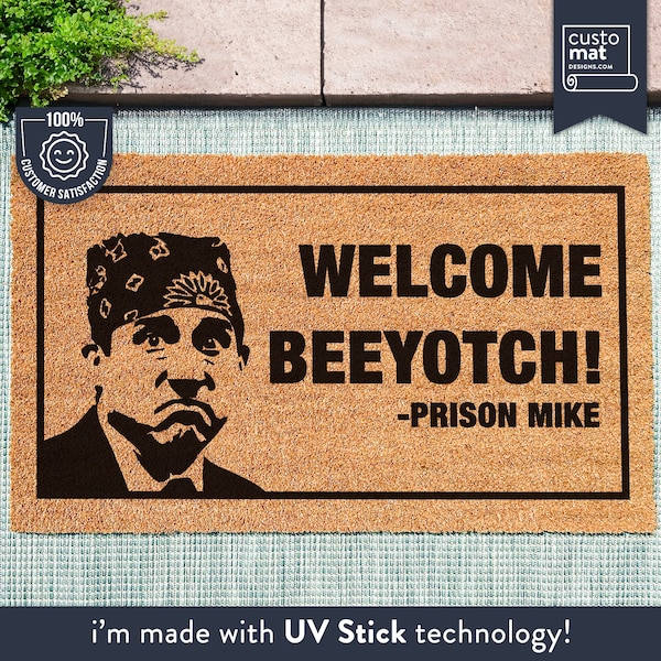 以下が含まれることがあります： 黒文字で「WELCOME BEEYOTCH! -PRISON MIKE」と書かれた茶色の玄関マット。マットの左側には、赤いバンダナを頭に巻いた男性の白黒イラストが描かれている。