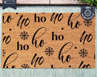 May include: A brown coir doormat with the words "ho ho ho" repeated in a black cursive font. The doormat also features a snowflake design.