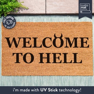 May include: A brown coir doormat with the text "WELCOME TO HELL" in black lettering. The "O" in "WELCOME" is replaced with a black devil's horns symbol. The doormat is made with UV Stick technology.