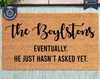 May include: A brown coir doormat with the text "The Boylstons Eventually. He just hasn't asked yet." in black lettering. The doormat is made with UV Stick technology.