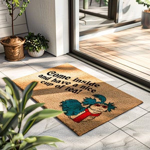 May include: A brown coir doormat with the text "Come inside and have a nice cup of tea!" in black. A blue and red cartoon creature is on the mat.