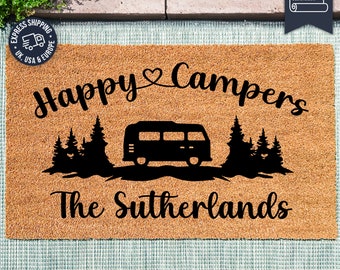 May include: A brown coir doormat with the text "Happy Campers" and a silhouette of a camper van and trees. The text "The Sutherlands" is below the camper van. The doormat is made with UV Stick technology.