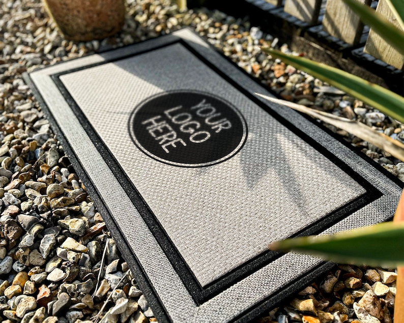 Puede incluir: Una alfombra de bienvenida gris con un borde negro y un c&iacute;rculo negro en el centro que dice "YOUR LOGO HERE".