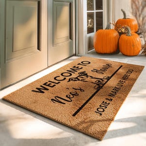 May include: A rectangular doormat with the text "WELCOME TO Neo's House" in black script. A graphic of a dog is in the center. The text "JOSIE & MARK LIVE HERE TOO" is at the bottom. Three orange pumpkins are in the background.