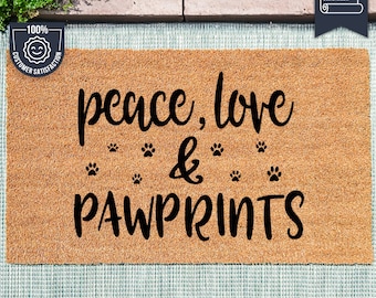 May include: A brown coir doormat with the text "peace, love & pawprints" in black lettering. The text is surrounded by paw print graphics. The doormat is made with UV Stick technology.