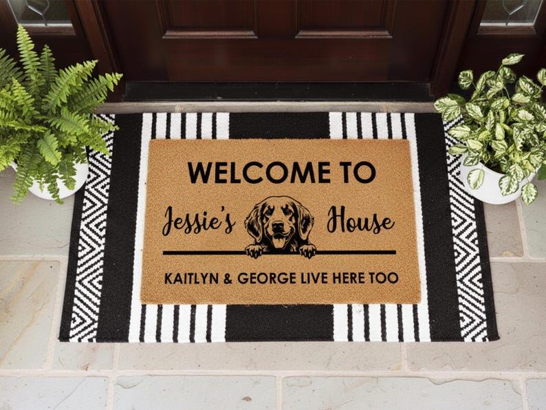 K&ouml;nnte beinhalten: Eine rechteckige Fu&szlig;matte mit dem Text "WELCOME TO Jessie's House" und einer Hunde-Grafik. Die Matte ist braun mit schwarzem Text und einem schwarz-wei&szlig; gestreiften Rand. Der Text "KAITLYN & GEORGE LIVE HERE TOO" ist ebenfalls enthalten.