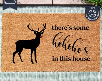 May include: A brown coir doormat with the text "there's some hohoho's in this house" and a black silhouette of a reindeer with a red nose. The doormat is made with UV Stick technology.