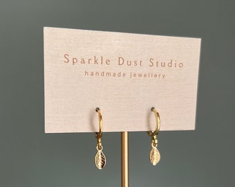 Può includere: Orecchini a forma di foglia dorati su una carta che recita "Sparkle Dust Studio handmade jewellery"
