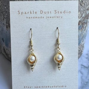 May include: Gold-coloured seashell earrings, each with a pearl centre. The earrings are displayed on a white card with the text "Sparkle Dust Studio handmade jewellery" and "Etsy: sparkleduststudio".