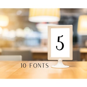 May include: A white table number holder with a black number 5 on a white card. The holder is on a wooden table. The text "10 FONTS" is below the holder.