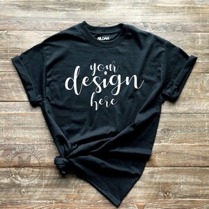 May include: Black t-shirt with rolled up sleeves, laying on a wooden surface. The shirt has the text "your design here" printed on the front in white.