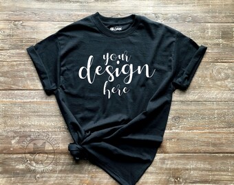 Puede incluir: Camiseta negra con mangas arremangadas, sobre una superficie de madera. La camiseta tiene el texto "your design here" impreso en blanco en la parte delantera.