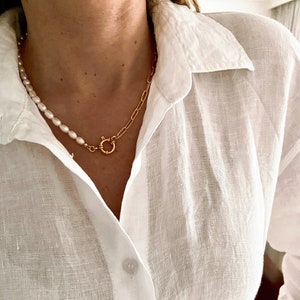 May include: A white linen shirt with a gold chain and pearl necklace. The necklace has a gold clasp.