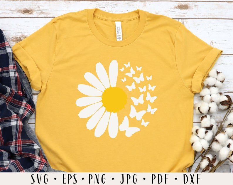 May include: A yellow t-shirt with a white daisy and butterflies design. The daisy has a yellow center and the butterflies are scattered around the daisy.