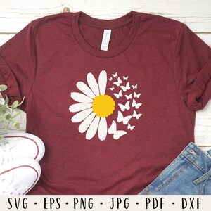 May include: A maroon t-shirt with a white daisy and white butterflies around it. The daisy has a yellow center.