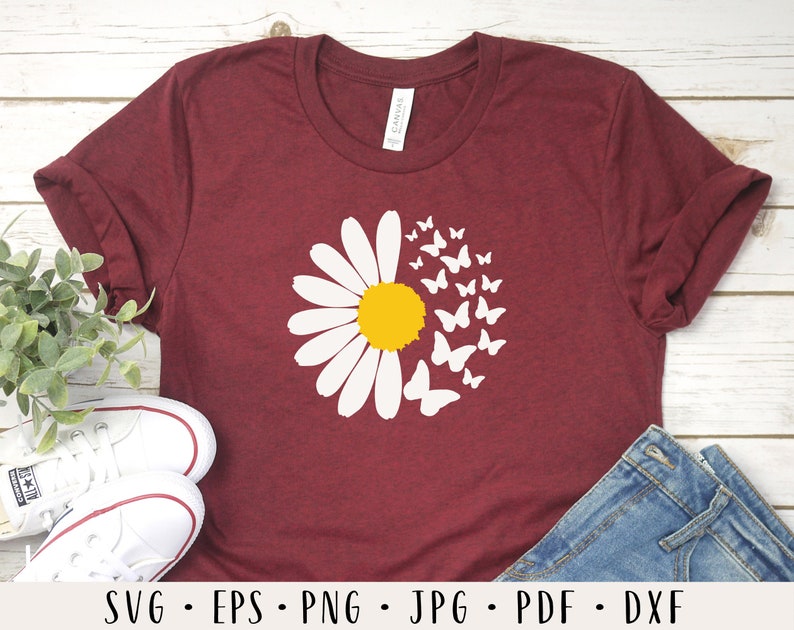 May include: A maroon t-shirt with a white daisy and white butterflies around it. The daisy has a yellow center.