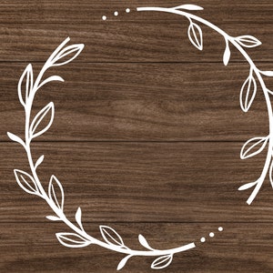 May include: A white outline of a wreath with leaves on a brown wood background.