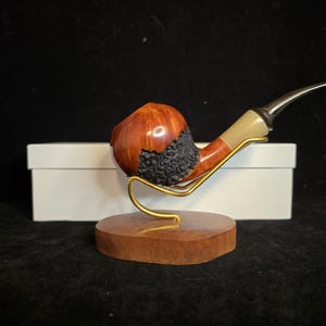 Peut inclure: Une pipe en bois avec une coupe noire et brune et un tuyau blanc. La pipe est sur un support en bois avec une base en métal doré.