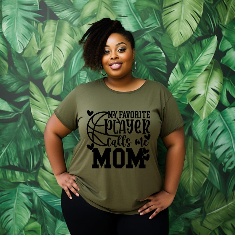 May include: A woman wearing a green t-shirt with a black basketball graphic and the text "My Favorite Player Calls Me Mom".