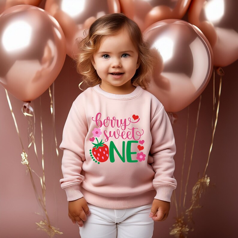 Puede incluir: Una sudadera rosa con el texto "berry sweet one" en letras verdes y rosas. Una fresa roja con hojas verdes est&aacute; al lado de la palabra "one".