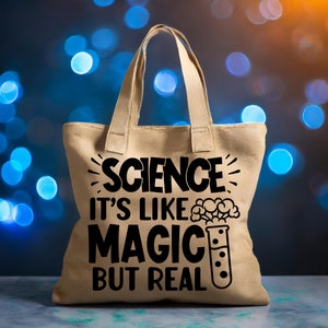 May include: A beige tote bag with black text that reads "Science it's like magic but real". The text is surrounded by a stylized sunburst design. A cartoon beaker with a bubbling potion is next to the text.