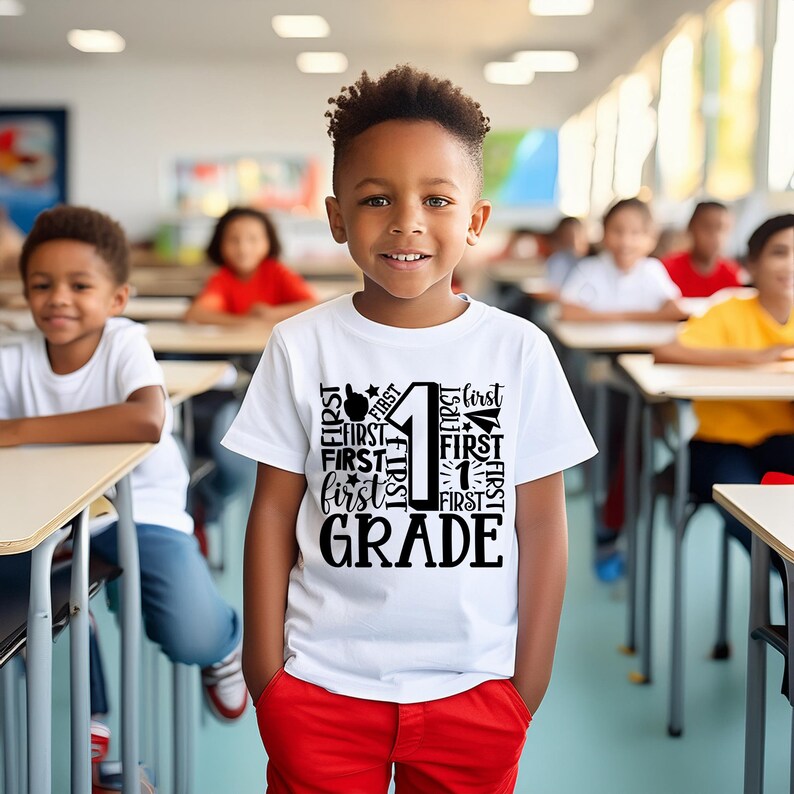 May include: A white t-shirt with a black graphic design featuring the number "1" surrounded by the word "first" and the words "first grade". A young boy is wearing the shirt in a classroom setting.