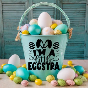 May include: A blue bucket filled with colorful Easter eggs. The bucket has a black vinyl decal that says "I'm a little eggstra".