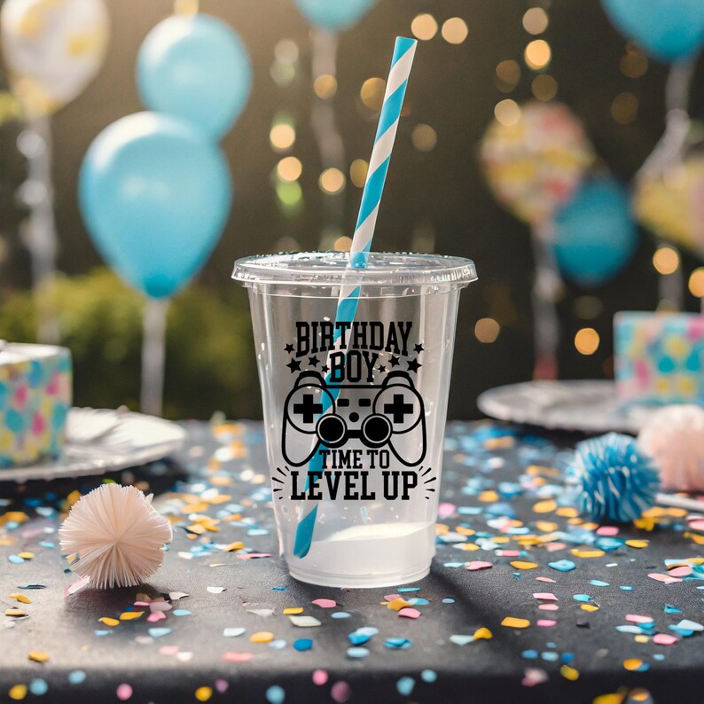 May include: A clear plastic cup with a black and white design that says "Birthday Boy" and "Time to Level Up" with a video game controller graphic. The cup has a blue and white striped straw.