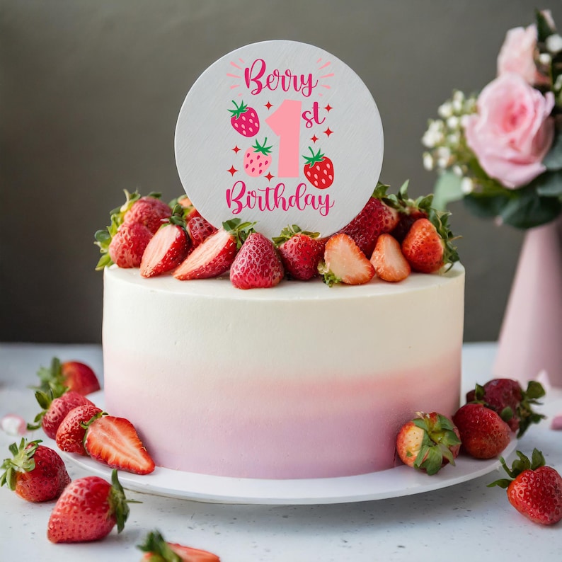 May include: A white and pink ombre cake decorated with fresh strawberries and a round cake topper that says "Berry 1st Birthday".