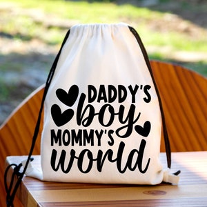 Pu&ograve; includere: Borsa a cordoncino bianca con testo nero che recita "Daddy's boy Mommy's world" con tre cuori neri.