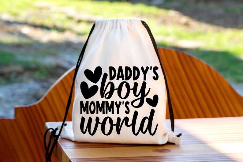 Pu&ograve; includere: Borsa a cordoncino bianca con testo nero che recita "Daddy's boy Mommy's world" con tre cuori neri.