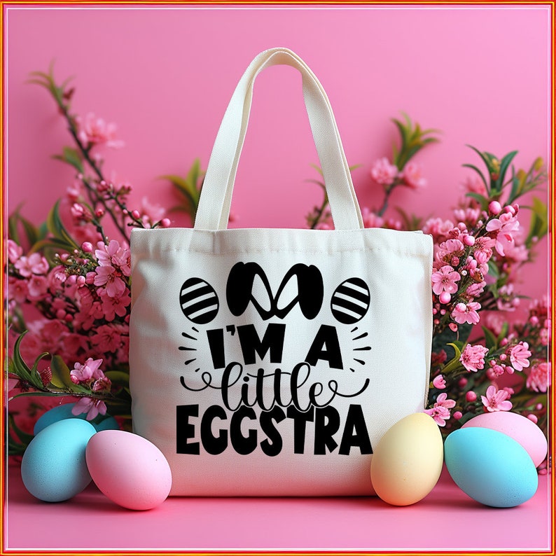 May include: A white canvas tote bag with black text that reads "I'm a little eggstra". The bag is surrounded by pastel-colored Easter eggs and pink flowers.