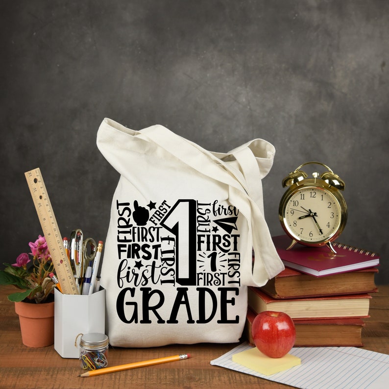 May include: A white canvas tote bag with a black design that says "First Grade" with the number 1 surrounded by the word "First" in different sizes and orientations.