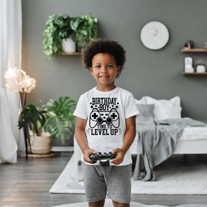 May include: A white t-shirt with a black graphic of a video game controller and the text "Birthday Boy Time to Level Up".