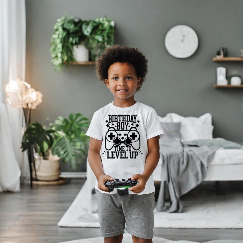 May include: A white t-shirt with a black graphic of a video game controller and the text "Birthday Boy Time to Level Up".
