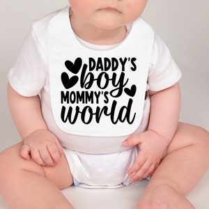 Pu&ograve; includere: Bavaglino bianco per neonato con testo nero che recita "Daddy's boy Mommy's world" con tre cuori neri.