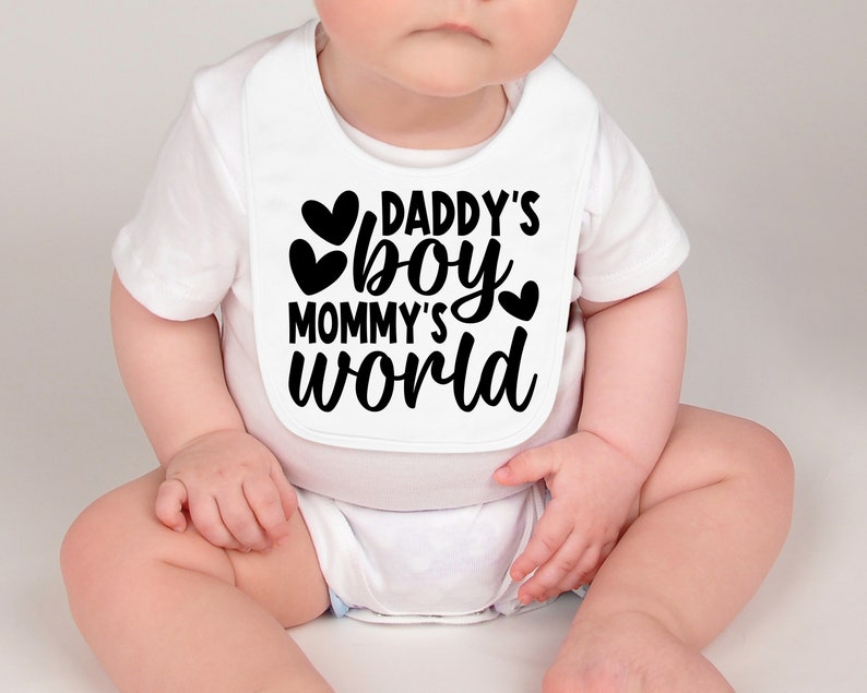 Pu&ograve; includere: Bavaglino bianco per neonato con testo nero che recita "Daddy's boy Mommy's world" con tre cuori neri.