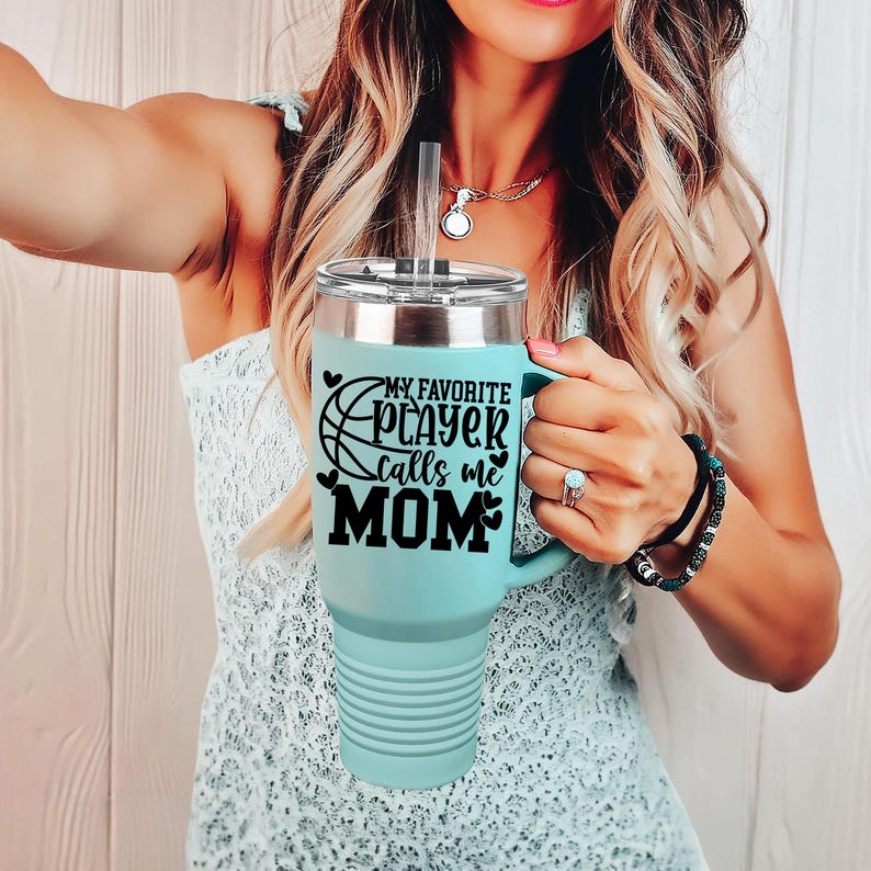 May include: A light blue stainless steel tumbler with a black vinyl wrap. The wrap features a basketball graphic and the text "My Favorite Player Calls Me Mom".