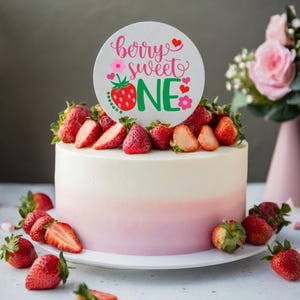 Puede incluir: Un pastel blanco y rosa degradado decorado con fresas frescas y un adorno redondo para pastel que dice "berry sweet one" en letras rosas y verdes con un gr&aacute;fico de fresa.