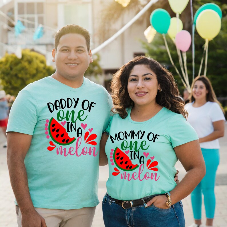 May include: A couple wearing matching light blue t-shirts with watermelon graphics and the text "Daddy of one in a melon" and "Mommy of one in a melon".