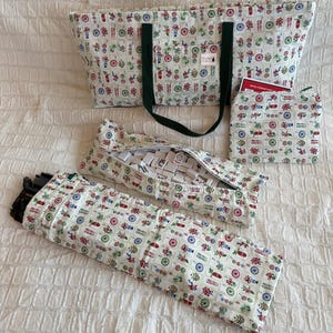 May include: A set of Mahjong game accessories, including a tote bag, tile cases, and a small pouch. The items are made of a cream-colored fabric with a repeating pattern of colorful floral and geometric designs. The tote bag has dark green handles.