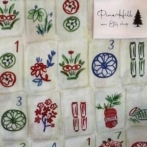 May include: Close-up of a fabric with a repeating pattern of Mahjong tiles. The tiles are white with colorful illustrations of flowers, circles, and bamboo. The text "Pine Hill an Etsy shop" is on a white label.